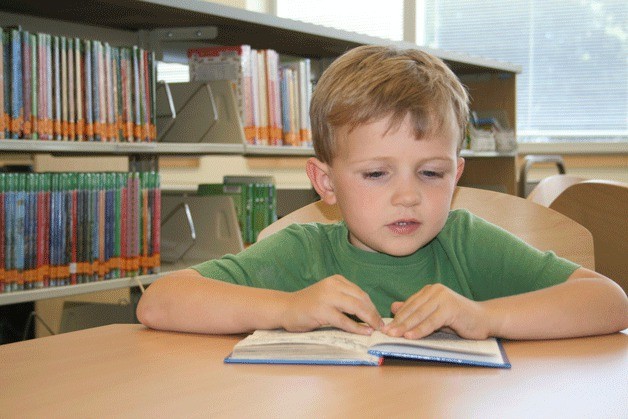 Gavin MacLean reads a book in the library of his new school Helen Keller Elementary.