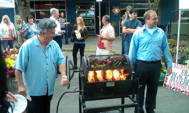 Pedro Escobar of Family Pepper & Produce roasts up some peppers as spectators look on during the Kirkland Wednesday Market on Wednesday. Escobar has been a KWM vendor for more than eight years.